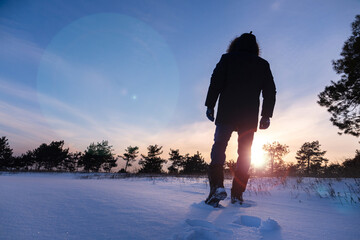 Silhouette of a person walking on the snow at sunset.
