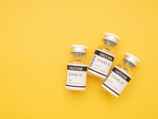 Top view of the covid-19 vaccine in glass bottles for prevention, immunization, and treatment from coronavirus infection on yellow background. Space for text. Concept of medical and vaccine