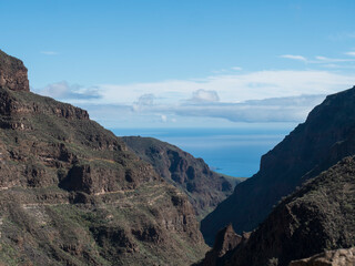 Barranco de Guayadeque view along the ravine steep walls towards ocean. Gran Canaria, Canary Island, Spain. Sunny day, blue sky, white clouds background