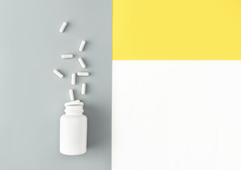 Mock-up bottle with spilled pills on isoleted white, trendy yellow and grey background. Cosmetology and medicine concept. Flat lay style.