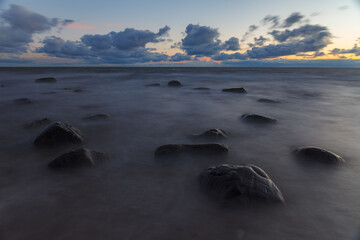 Fototapeta na wymiar Baltic sea stones at sunset. Waves over shallow water.