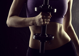 Slim athletic woman Holding dumbbell in the hand on black