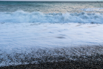 beautiful blue sea with waves, beach with rocks, sky at sunset