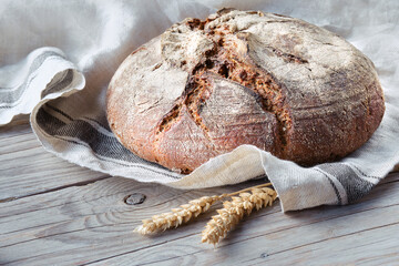 No knead handmade loaf on cutting board on wood with linen towel, spelt ears. German Bauernbrot...
