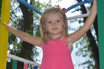 summer beautiful cute little blonde girl  in pink dress is playing on the playground
