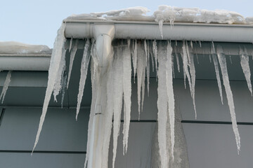 Icicles on the roof. The drain is full of snow and ice. Icicles falling danger concept.