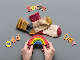 Odd Socks Day text. Pair of mismatched school socks on top of wooden rainbow. Hand holding the rainbow. Social initiative against bullying. Promotion design for anti-bullying campaign.
