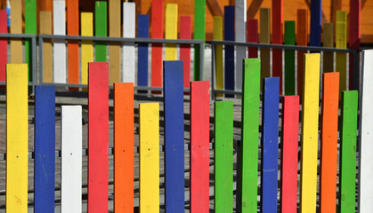 Wooden fence with multicolored planks built on a surface of concrete slabs.