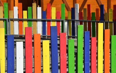 Wooden fence with multicolored planks built on a surface of concrete slabs.