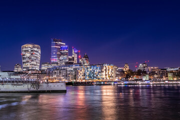 Fototapeta na wymiar London cityscape at night view at the City of London from across the river Thames, night life in UK capital city, lots of lights and reflections in the water and beautiful sky with long exposure photo