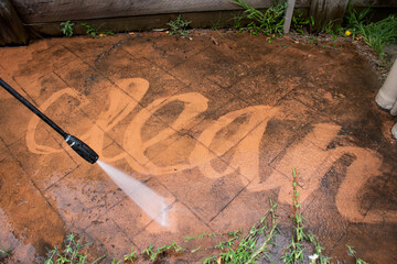 Cleaning backyard paving tiles with pressure washer.