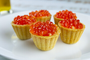 tartlets with red salmon caviar on a white plate, delicious appetizing baskets with eggs close-up on a white background