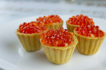 tartlets with red salmon caviar on a white plate, delicious appetizing baskets with eggs close-up on a white background