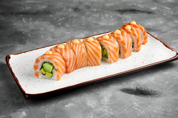 Classic red dragon sushi roll with avocado, salmon, omelette and spicy sauce on a white plate on a gray background. Selective focus, noise grain on post