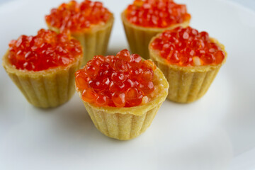 tartlets with red salmon caviar on a white plate, delicious appetizing baskets with eggs close-up on a white background