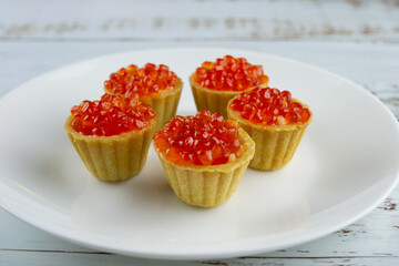 tartlets with red salmon caviar on a white plate, delicious appetizing baskets with eggs close-up on a white background