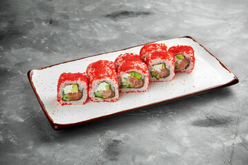 Classic sushi california roll in tobiko caviar with salmon, cucumber and cream cheese on a white plate on a gray background. Close up, selective focus