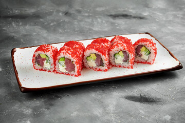 Classic sushi california roll in tobiko caviar with tuna, cucumber and cream cheese on a white plate on a gray background. Close up, selective focus