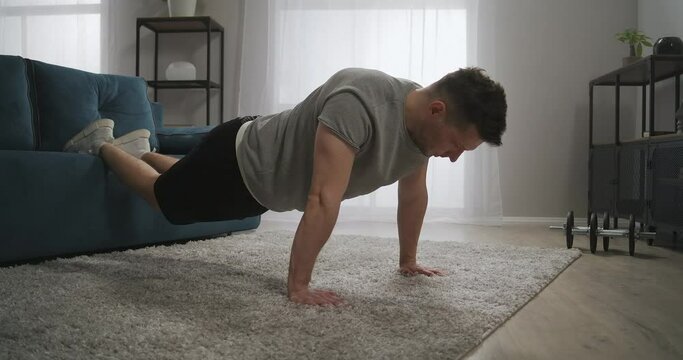 sporty man is training at home, doing push-ups in living room, workout at home, exercises for biceps, back and chest