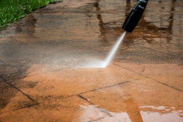 Cleaning backyard paving tiles with pressure washer.