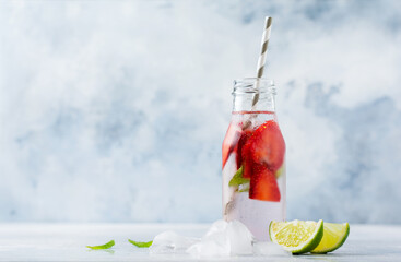 Summer lemonade with ice, strawberries, mint and lime in a bottle and a paper tube on a concrete...
