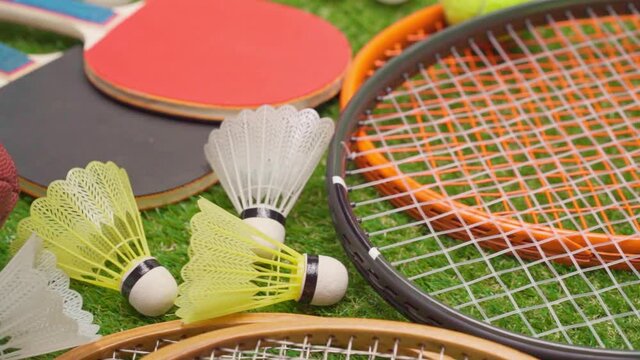 Various sport equipment on grass including rackets, balls, shuttlecocks and ball close up
