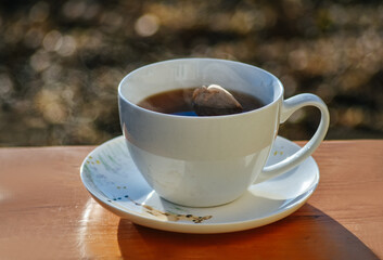 Hot tea cup on a frosty winter day put on wooden table with background of front garden in morning.