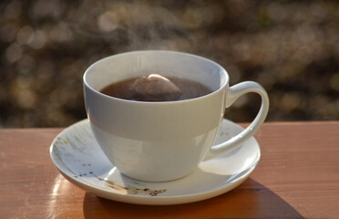 Hot tea cup on a frosty winter day put on wooden table with background of front garden in morning.