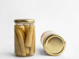 Glass jars with pickled baby corn on white background