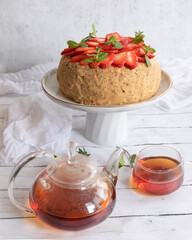 Homemade honey cake with fresh berries and tea on a light background.