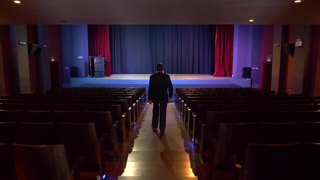 A Politician walks the corridor of a theater where the chair of power is waiting for him on the stage, metaphorically 