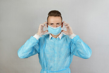 A blond male surgeon in a blue uniform, wearing protective transparent gloves, wearing a medical mask. Health care, stay at home. A brutal Caucasian doctor, in a medical gown and gloves. Copyspace.