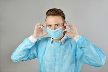 A blond male surgeon in a blue uniform, wearing protective transparent gloves, wearing a medical mask. Health care, stay at home. A brutal Caucasian doctor, in a medical gown and gloves. Copyspace.