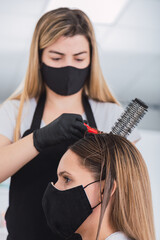 Fototapeta premium Pretty hairdresser with black protective mask and latex gloves - Hairdresser styling a young woman wearing a protective mask.