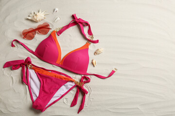 Stylish swimsuit and sunglasses on sand, flat lay with space for text. Beach accessories