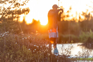 man making photo on SUP stand up paddle boarding at sunset in lake. Summer evening activity