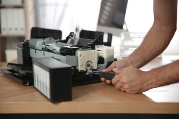 Repairman with screwdriver fixing modern printer indoors, closeup