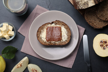 Bread with butter and quince paste on black table, flat lay