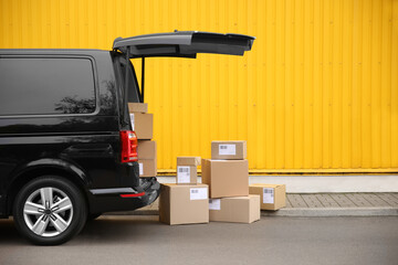 Black delivery van and many different parcels near yellow building outdoors, space for text....