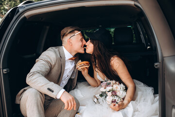 The newlyweds have a delicious hamburger and fries in the trunk of the car.