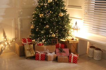 Gift boxes under Christmas tree with fairy lights indoors