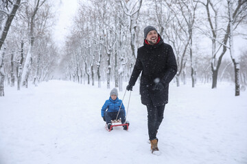 Fototapeta na wymiar Father sledding his child outside on winter day. Christmas vacation