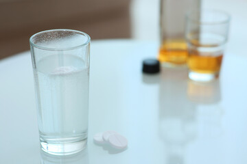 Glass of hangover remedy and pills on table indoors. Space for text