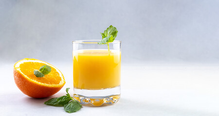 Fresh oranges and orange juice in glasses on an orange background. Mint leaves. Still life. Close up. Copy space.