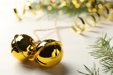Golden sleigh bells and fir branch on white table, closeup - Powered by Adobe