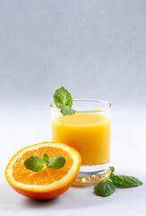Fresh oranges and orange juice in glasses on an orange background. Mint leaves. Still life. Close up. Copy space.