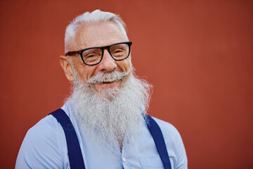 Cheerful hipster man in welcoming mood posing on red wall background - Fashionable person in casual fashion clothes - Happy elderly lifestyle concept with no age limit