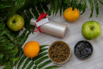 image of homemade cosmetics ingredients. aroma theme. Black mask, clay. organic cosmetics with extracts of herbs apples, lemons and oranges on white leaf green background