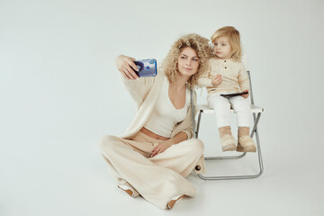 Blonde young Caucasian mother with daughter trying to make selfie photo on smartphone on white background isolated - 410931690