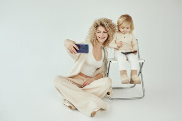 Blonde young Caucasian mother with daughter trying to make selfie photo on smartphone on white background isolated - 410931698